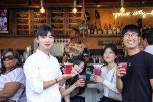 Three people standing in front of a bar, smiling and holding red drinks