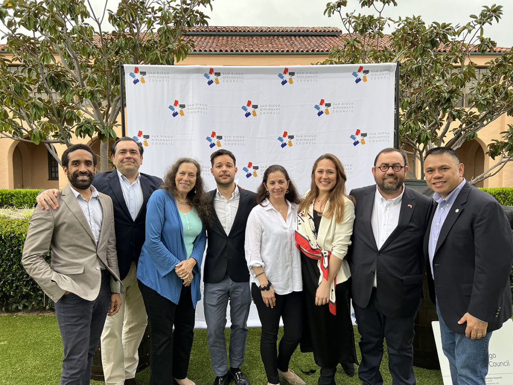 A group of people pose in front of a banner at a San Diego Diplomacy Council event.