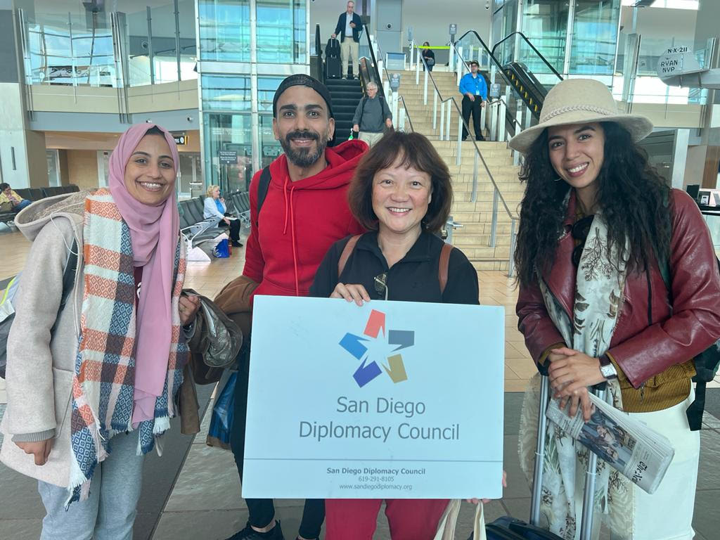 A group of hosts wait at the airport with a San Diego Diplomacy Council sign.