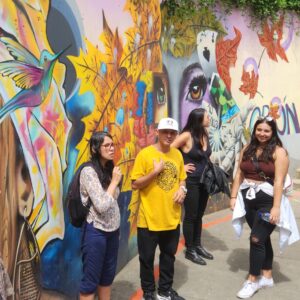 A group of people stand in front of a colorful mural during a tour of Columbia.