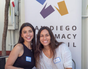 Lulu and Adrianna, two San Diego Diplomacy employees, pose together in front of the Diplomacy Council banner.